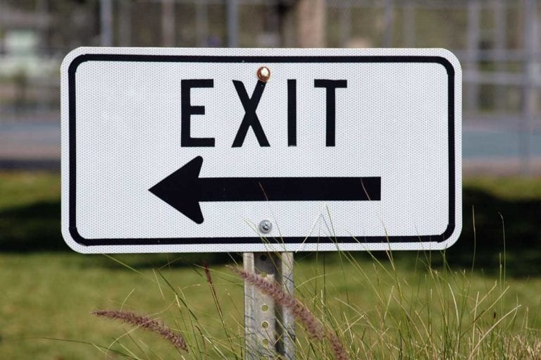 An exit road sign next to a green lawn.