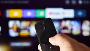 Mão segurando controle remoto, escolhendo plataforma de streaming.