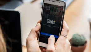 Mão segurando celular com imagem da tela de acesso ao Tela Brasil