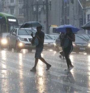Pedestres atravessam uma rua sob chuva intensa em São Paulo, usando guarda-chuvas, enquanto carros e um ônibus circulam pela via molhada.