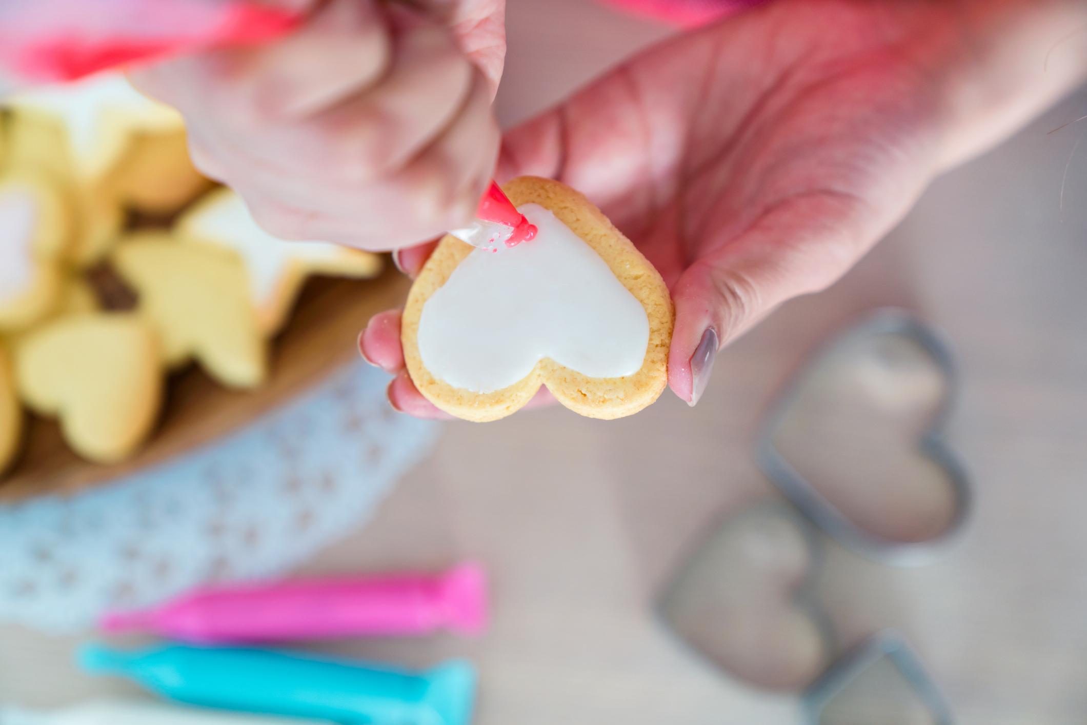 Overhead view of a woman icing a heart shaped cookie