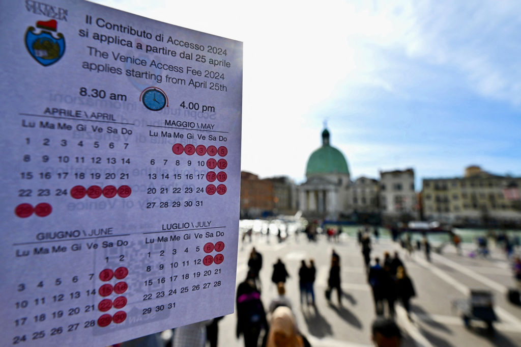 Eine Person zeigt einen Kalender der zahlungspflichtigen Tage für einen Besuch in Venedig am 19. April 2024 vor dem Bahnhof Santa Lucia in Venedig. 