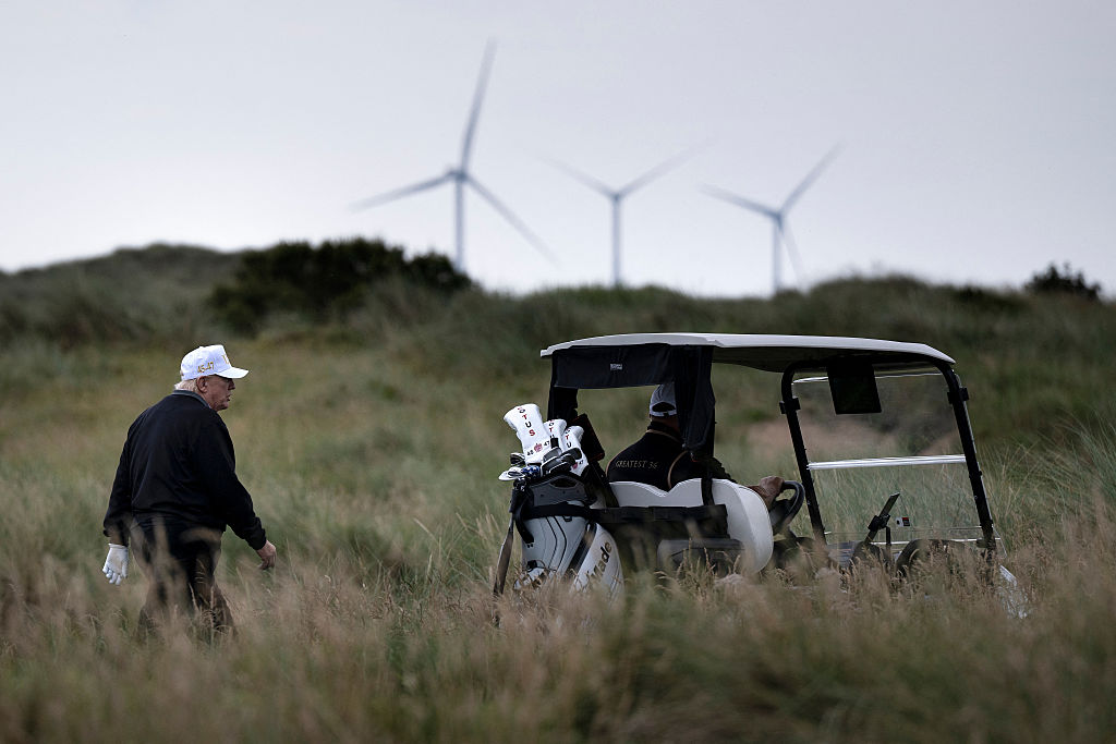 Trump walking on a golf course with wind turbines offshore in the background