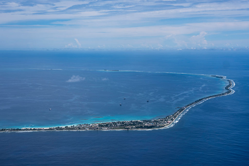 Funafuti, Tuvalu is seen from an airplane. The island is narrow and surrounded by azure sea.