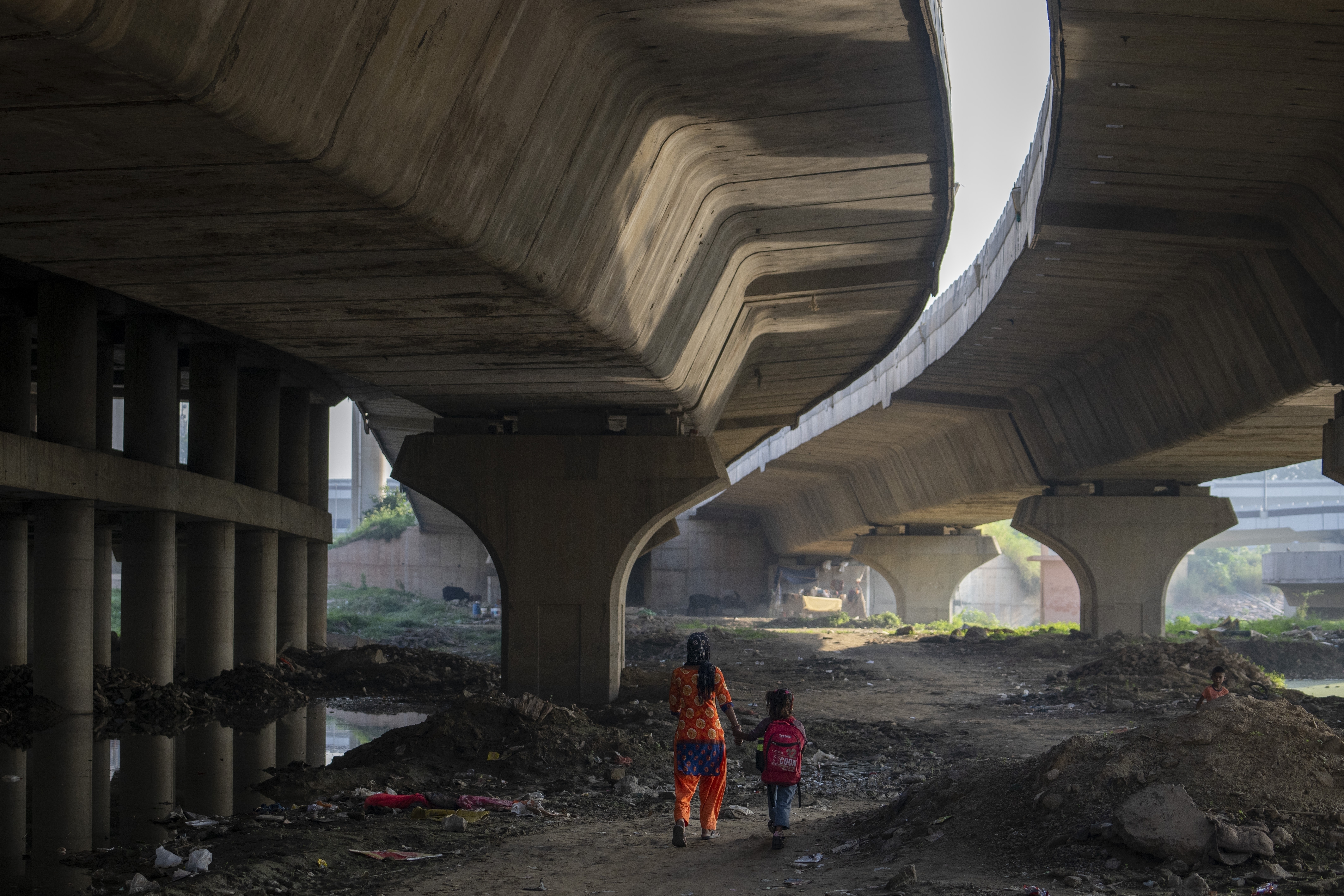 Meera Devi, left, accompanies her daughter Arima, 7, to her school as they walk on the flood plain of Yamuna River, in New Delhi, India, Friday, Sept. 29, 2023. Their family was among those displaced by the recent floods in the Indian capital's Yamuna River.