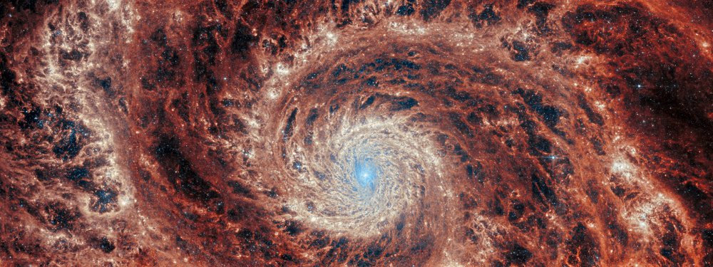 Ang pananaw sa gitna ng infrared ng Webb ng galaxy M51. Isang malaking spiral na galaxy ay tumatagos sa buong larawan. Ang core ay karamihan ay maputing puti, ngunit mayroon din umiikot na mga istrakturang katulad ng tubig na naglilinya sa paligid ng isang drain. May maputing liwanag at mapilak na asul na lumalabas mula sa mga bituin at alikabok sa gitna ng core, ngunit ito ay mahigpit na limitado sa core. Ang mga detalyadong singsing ay may mga pita ng malalim na dilaw at mapaklaum na abo, na pinaghihiwalay ng mas madilim na walang laman na mga rehiyon sa buong.