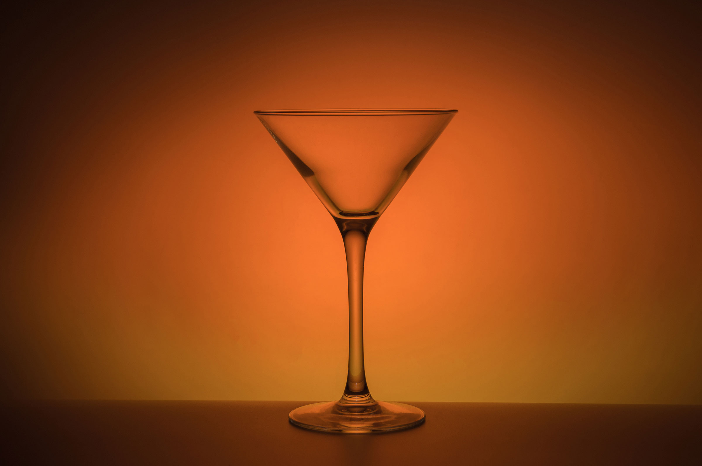 An empty transparent martini glass on a moody orange background