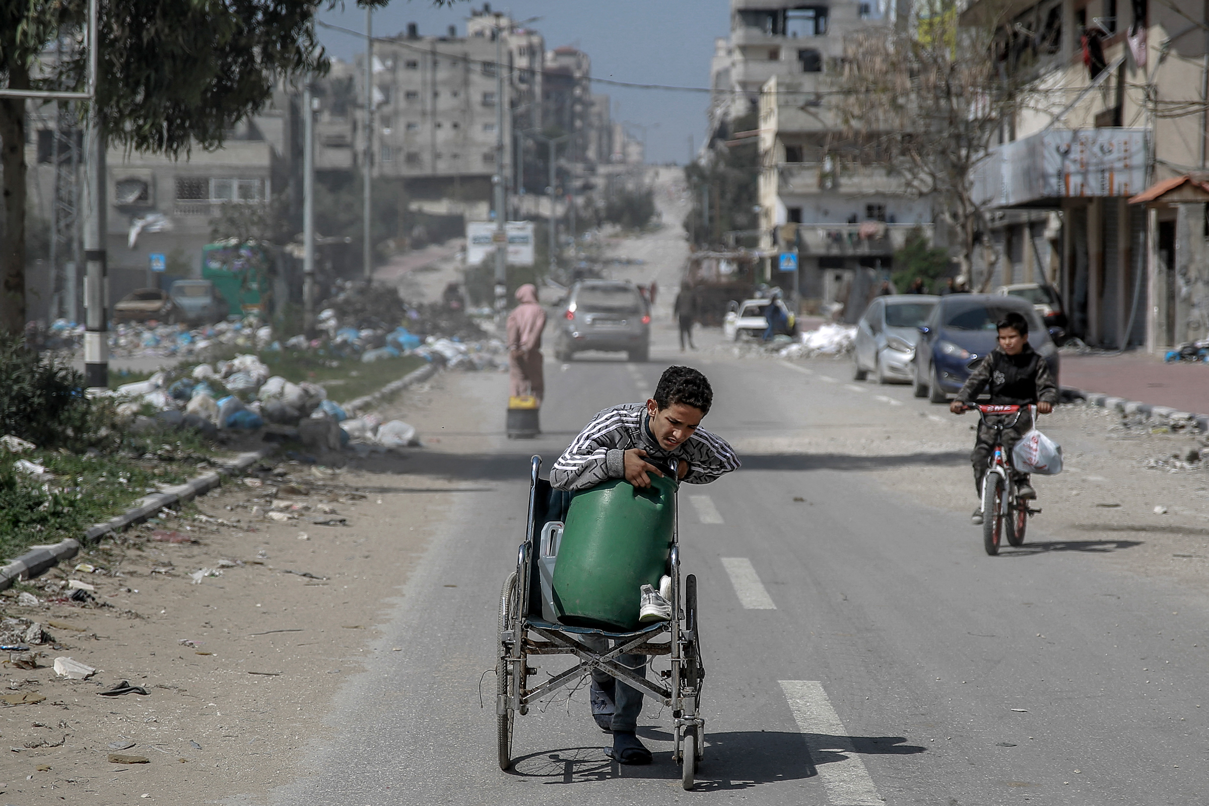 Isang batang lalaki ay nagdadala ng isang container ng tubig sa isang wheelchair sa loob ng kalye sa Lungsod ng Gaza noong Marso 3, sa gitna ng patuloy na hidwaan sa pagitan ng Israel at Hamas.