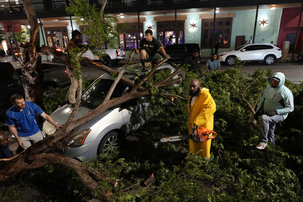 Nghệ sĩ Trae tha Truth, mặc áo vàng, cắt những cành cây đổ trên nóc chiếc xe sau cơn bão mạnh đi qua trung tâm thành phố vào Thứ Năm, ngày 16 tháng 5 năm 2024, tại Houston.