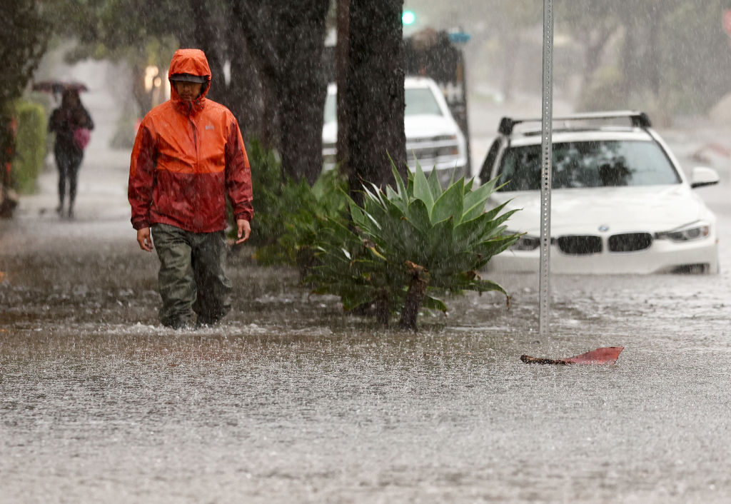 一個人走在淹水的街道上，2024 年 2 月 4 日，第二場低於一周時長的強勁持續性大氣河流風暴影響加州聖塔芭芭拉。  