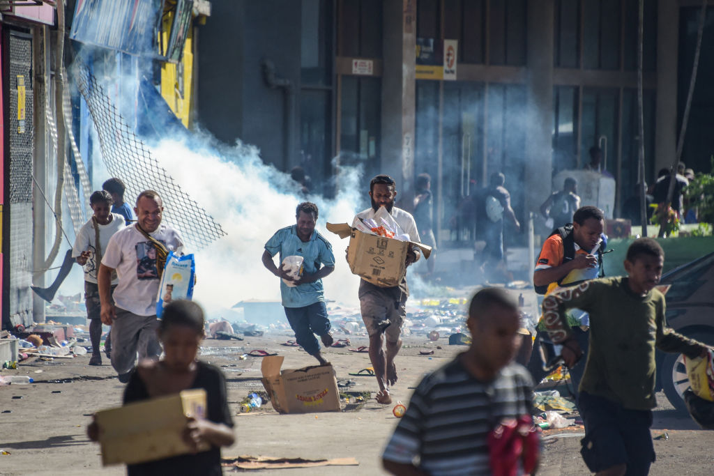 Orang berlari dengan barang dagangan ketika orang ramai meninggalkan kedai dengan barang rampasan di tengah keadaan tidak tenang di Port Moresby pada 10 Januari 2024.