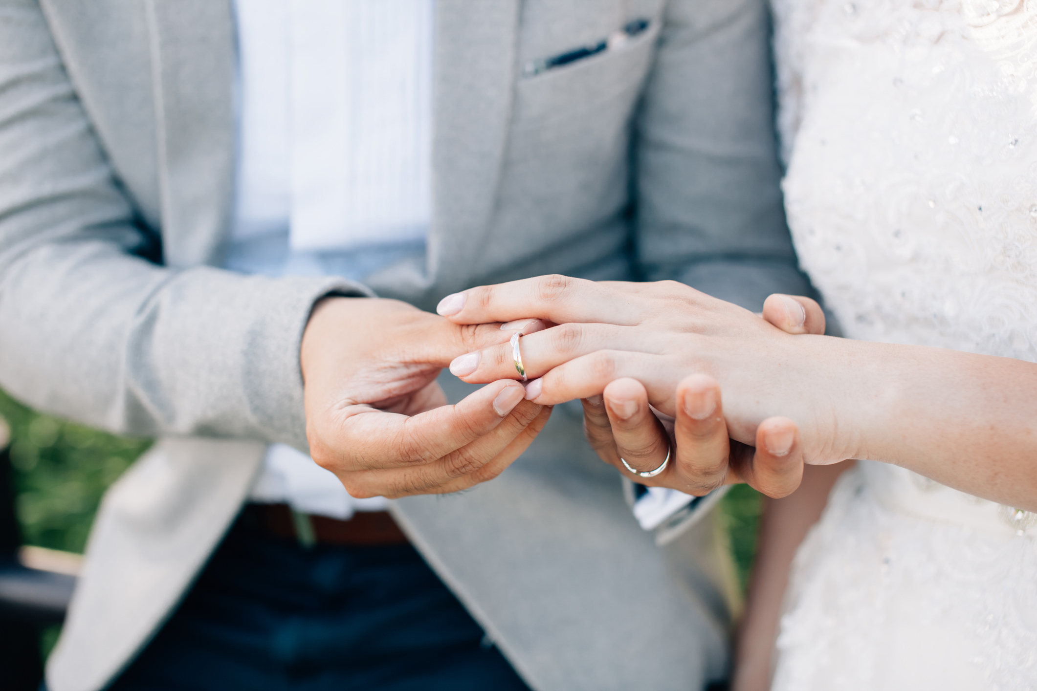 Groom putting ring on bride's finger. Rings exchange. Happy couple celebrating wedding outdoors.