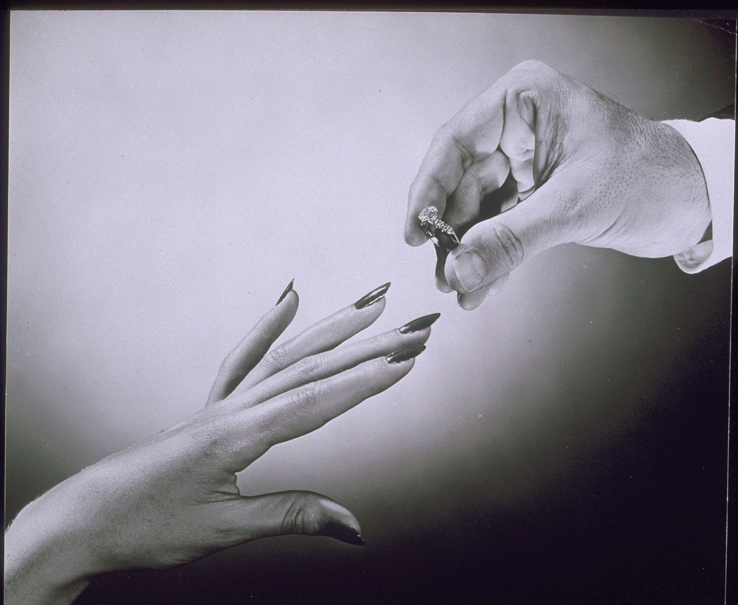 黑白影像中，一隻手為另一隻手戴上結婚戒指