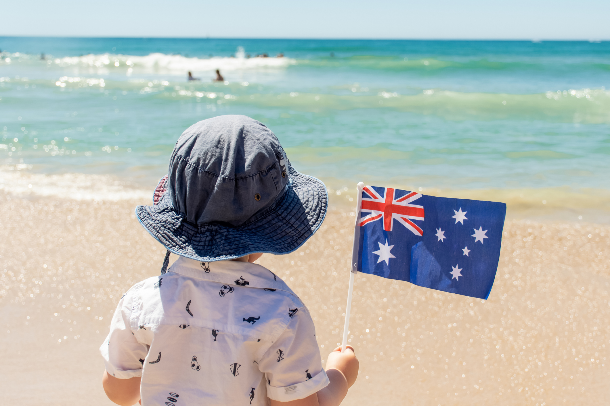 小男孩戴著帽子，在一個沙灘上拿著澳洲國旗。澳洲國慶日的概念