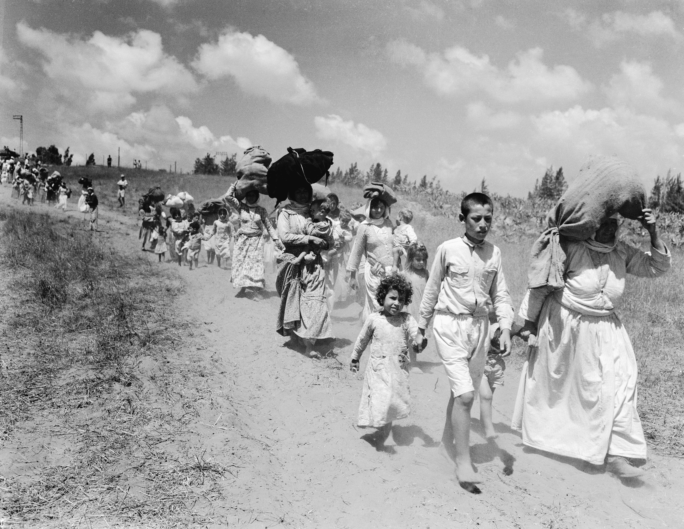 Arab refugees, mostly women and children, from village near Haifa begin a three mile hike carrying large bundles of personal possessions to the Arab lines in Tulkarim, West Bank, on June 26, 1948.