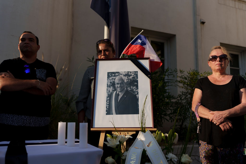 Supporters of former President of Chile Sebastián Piñera stand next to a photo with a Chilean flag during a memorial service for party member and former Chilean President Sebastián Piñera at Renovación Nacional headquarters on Feb. 6, 2024 in Santiago, Chile.