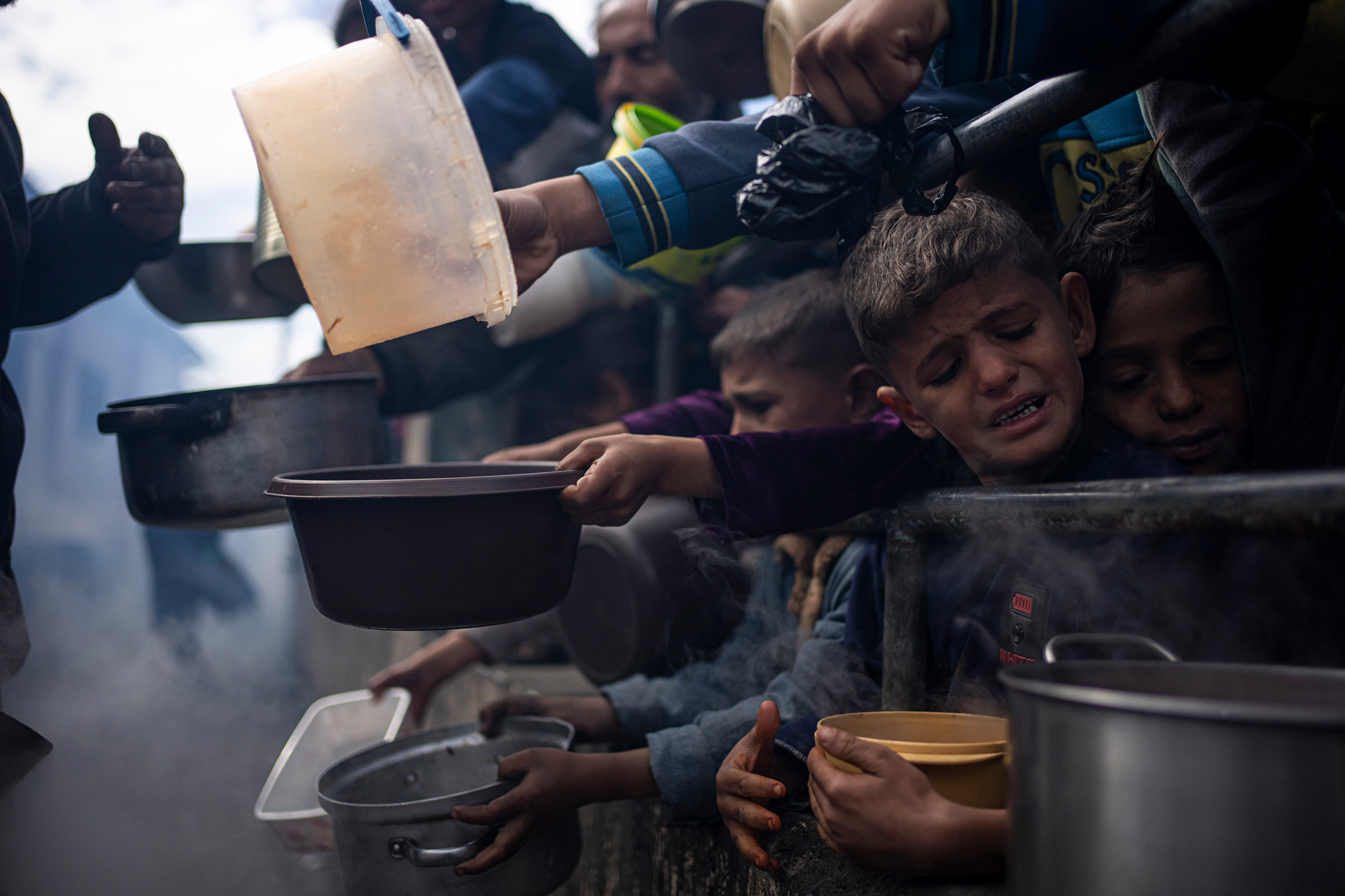 2024年2月16日,巴勒斯坦拉法市的难民营中,有人在世界粮食计划署提供的免费餐中排队。世界粮食计划署周二表示,由于加沙地区日益混乱,它已经暂停向孤立的北加沙地区提供食物援助,这加剧了可能发生饥荒的担忧。
