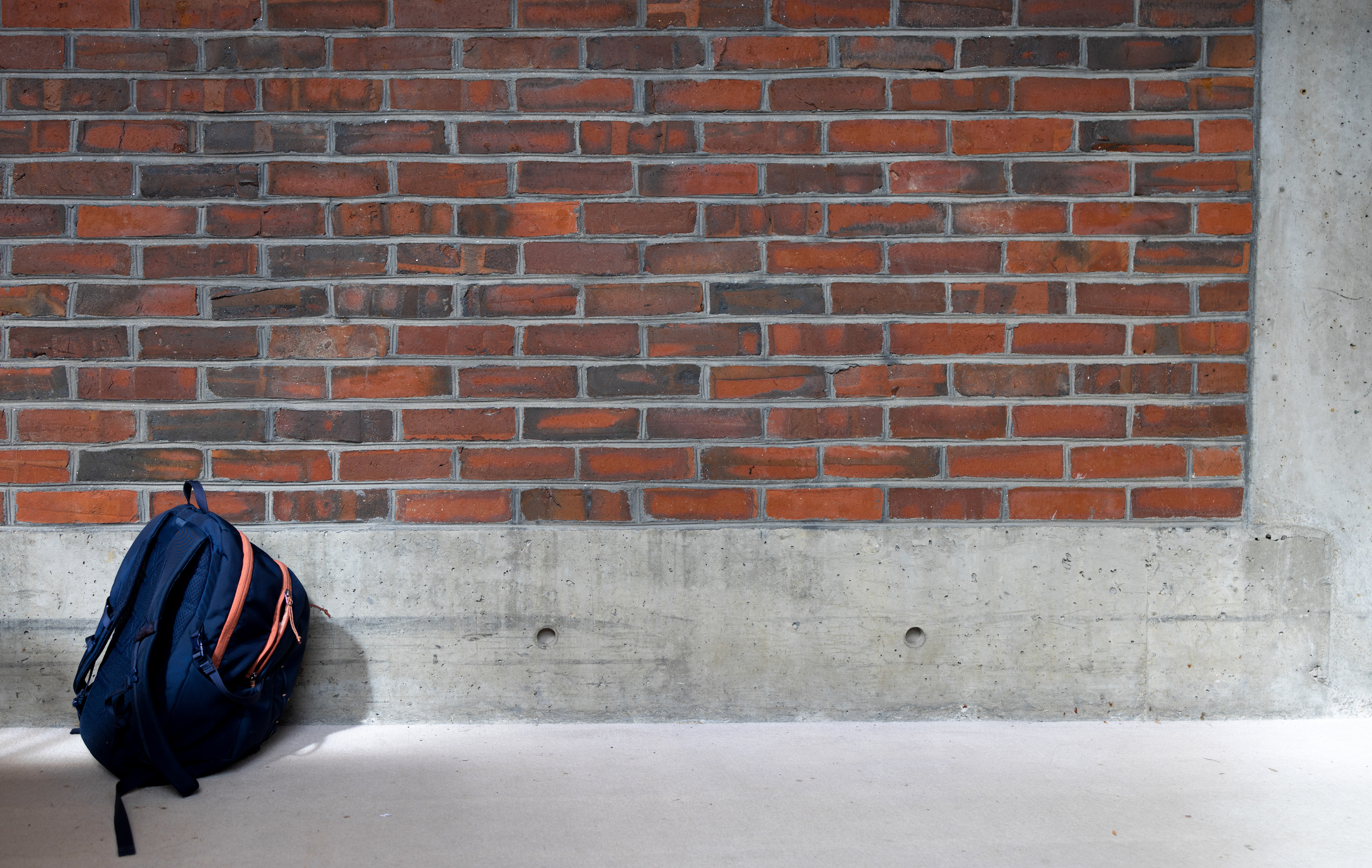 single student backpack in front of brick wall
