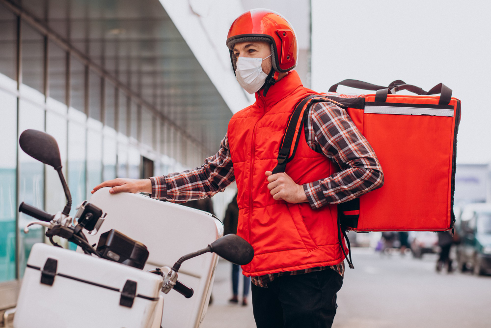 food delivery boy driving scooter with box with food wearing mask