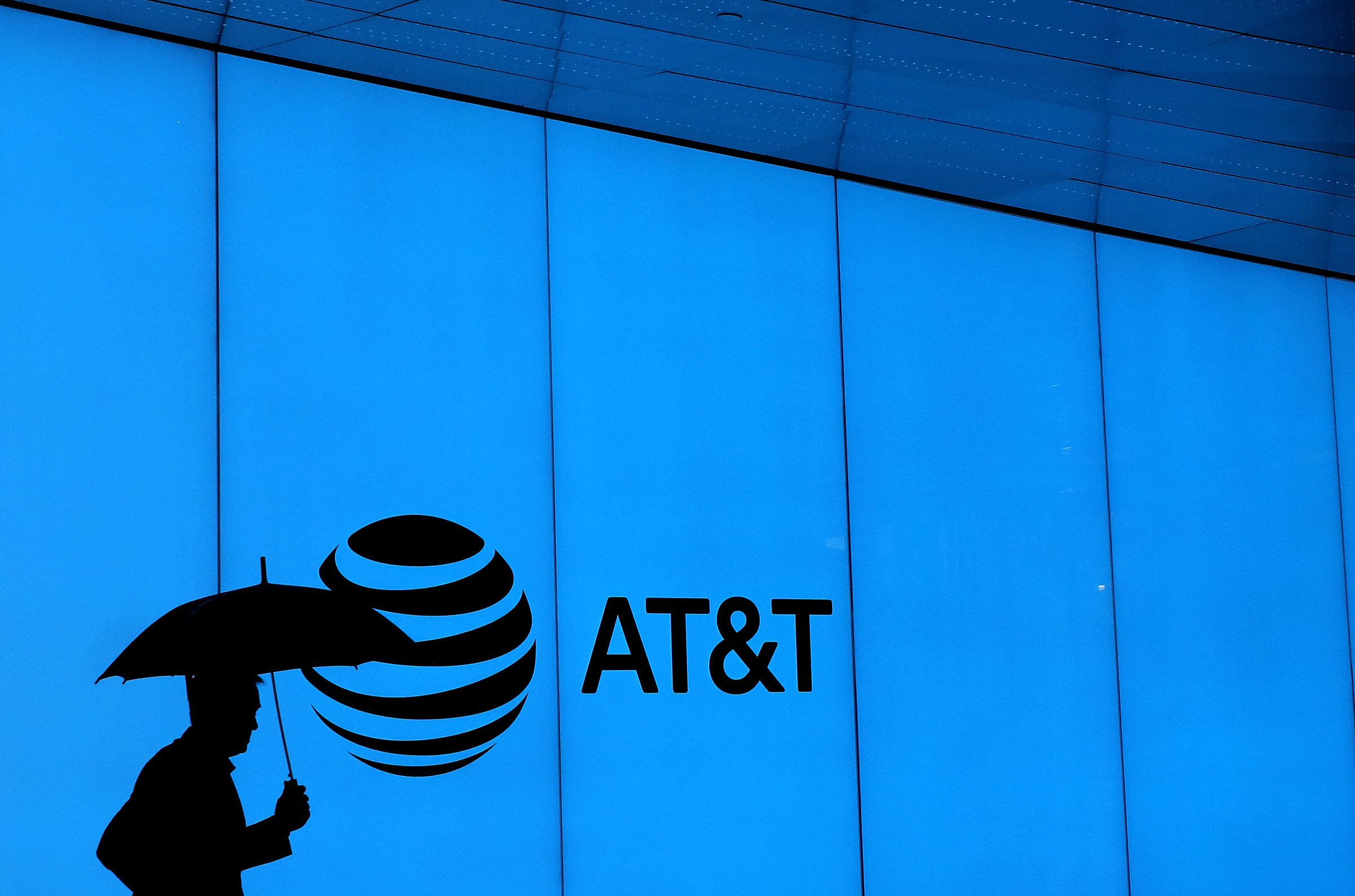 拿著雨傘的男子剪影，背對藍色牆壁，牆面上印著 AT&T 的標誌