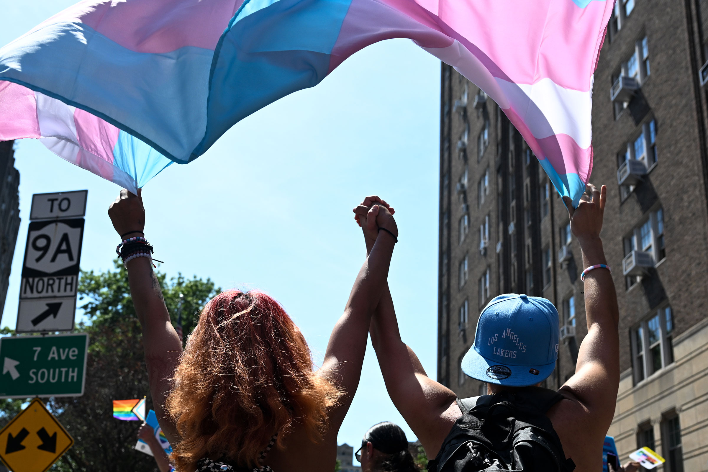兩個人在紐約市驕傲遊行中手牽手行走,背景是彩虹驕傲旗。