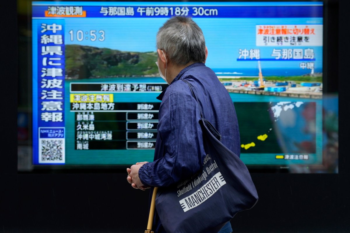 一個人站在人行道上，觀看電視上沖繩海嘯的突發新聞