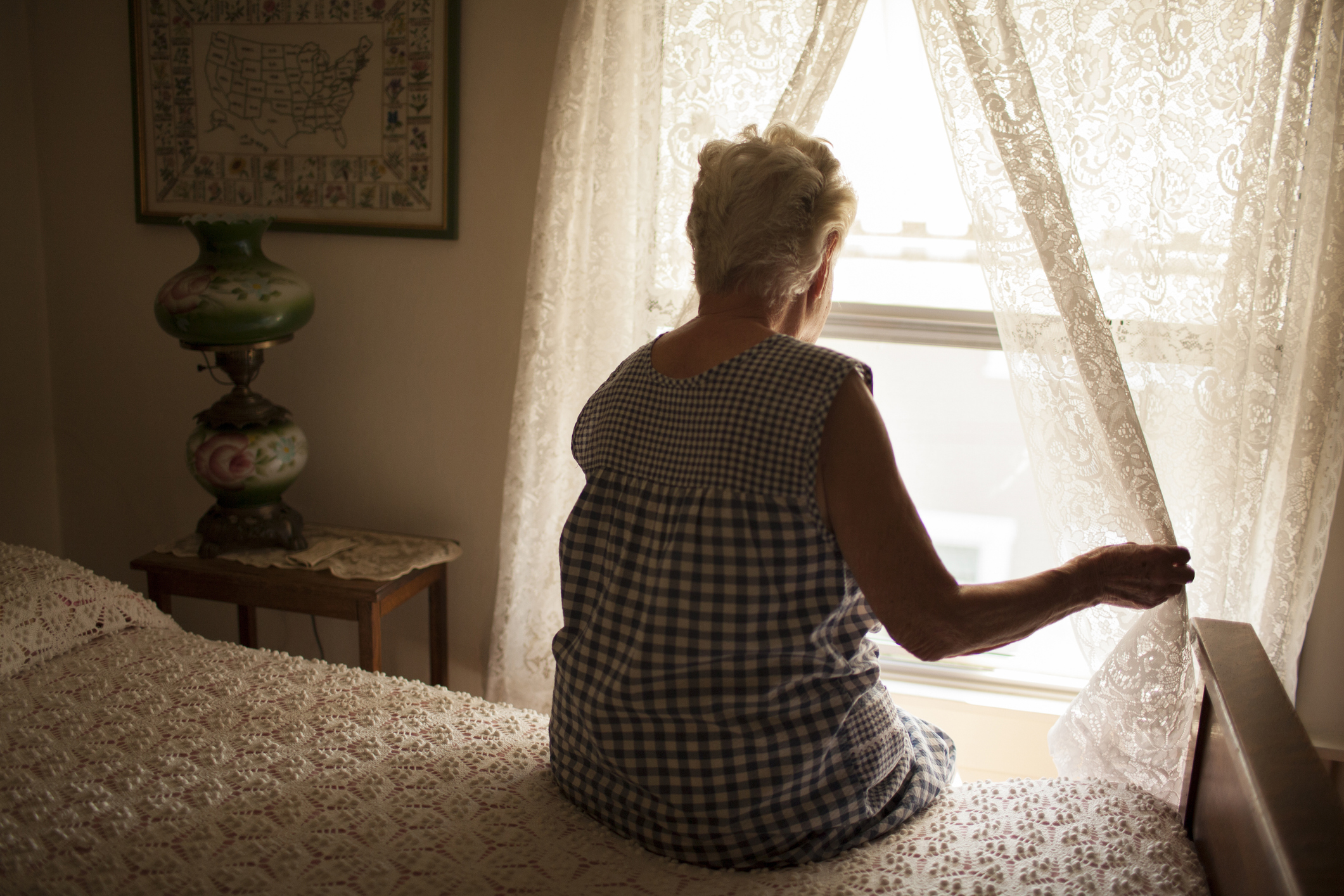 Người phụ nữ lớn tuổi suy nghĩ nhìn ra cửa sổ phòng ngủ