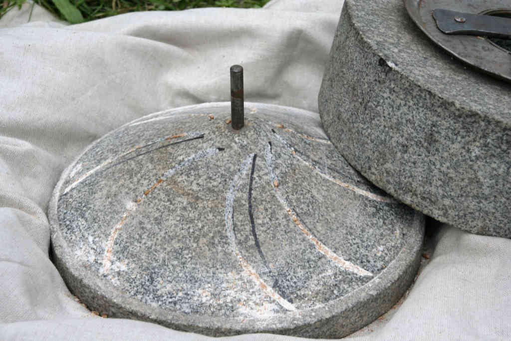 Deux meules en pierre d’un moulin à main romain sur un tissu blanc, elles sont faites de granit et ont des rainures sur la surface et une tige métallique au centre pour celle du dessous