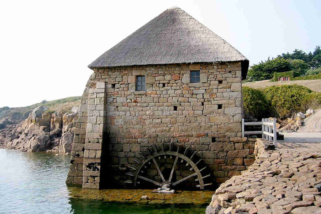 Moulin à marée du Birlot à l'ouest de l'île de Bréhat en Bretagne, très ensoleillé, toit en chaume avec des murs en pierre de moellon et une roue à Aubes