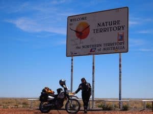 Danielle Murdoch on the first leg of her epic Australia, Africa, Europe and back trip. She is standing in front of the Northern Territory border sign. The sun is shining, it is hot and she is in full motorcycle gear. © Danielle Murdoch http://motomonkeyadventures.com/