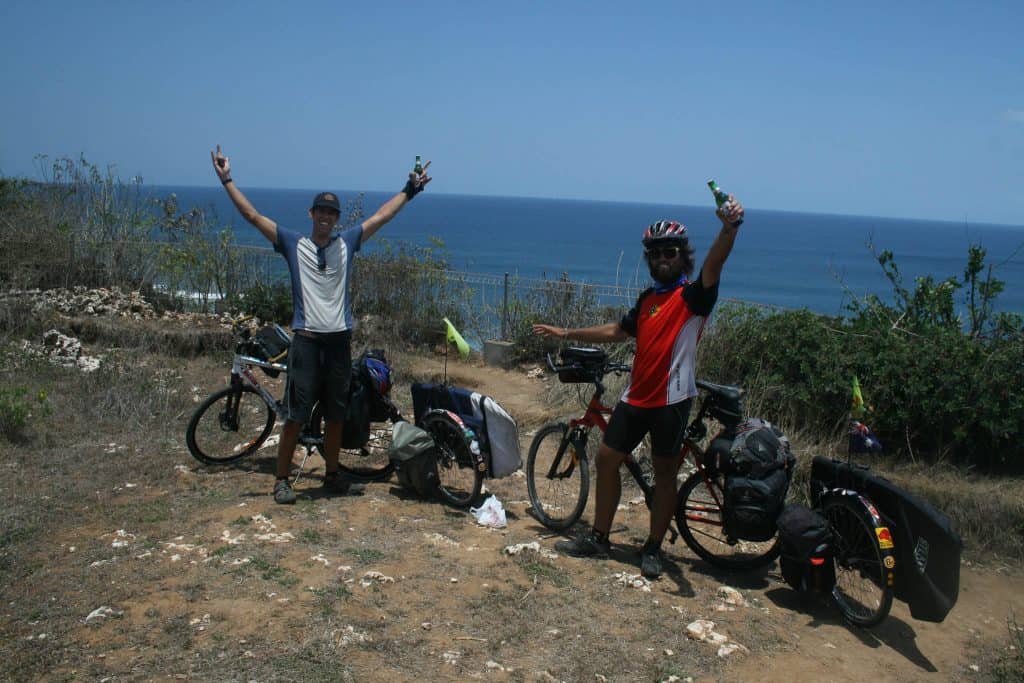 The Horizontal photo shows Rian and Dylan standing with their bicycles on the cliff of Uluwatu, Bali, Indonesia. They have cycled Indonesia from North to South and are celebrating their successful journey. Dylan is holding both arms up as a victory sign. Rian has got one arm up. He is holding a beer. Rian is wearing the Australia Flag Original Buff® as neck cooler. It appears mid day with hardly any shadow and a clear blue sky. It must be hot. Source: Eatsleepsurf.com.au Copyright: Unknown. We received the images as "Thank You" for providing the Buff®