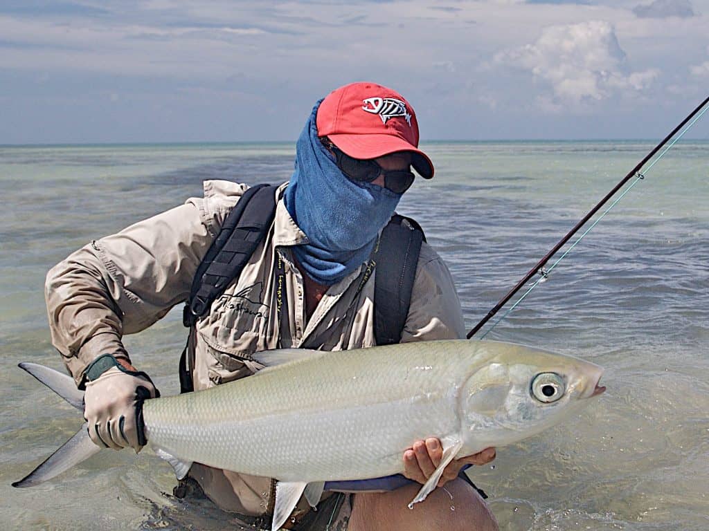 A frontal landscape shot of a fly fisherman standing up to his hips in water. The man is holding a large milkfish in his hands. He is wearing a High UV Buff® as face mask. Addional cap, long sleeve shirt and cap indicate that he wants total UV protection. Source: buff.eu Copyright: ©2007 Pat Ford. Given to us for the promotion of the High UV Buff® in the fishing market