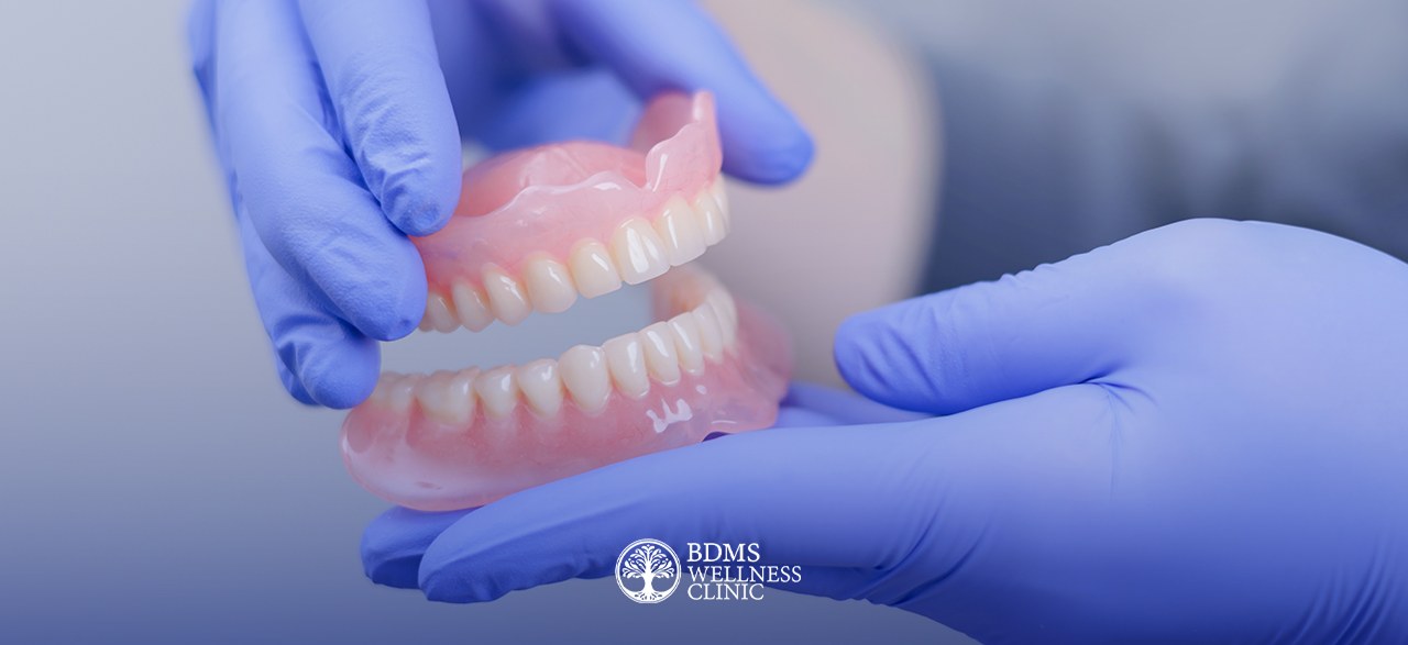 Dentist holding a set of full upper and lower dentures at BDMS Wellness Clinic, Bangkok