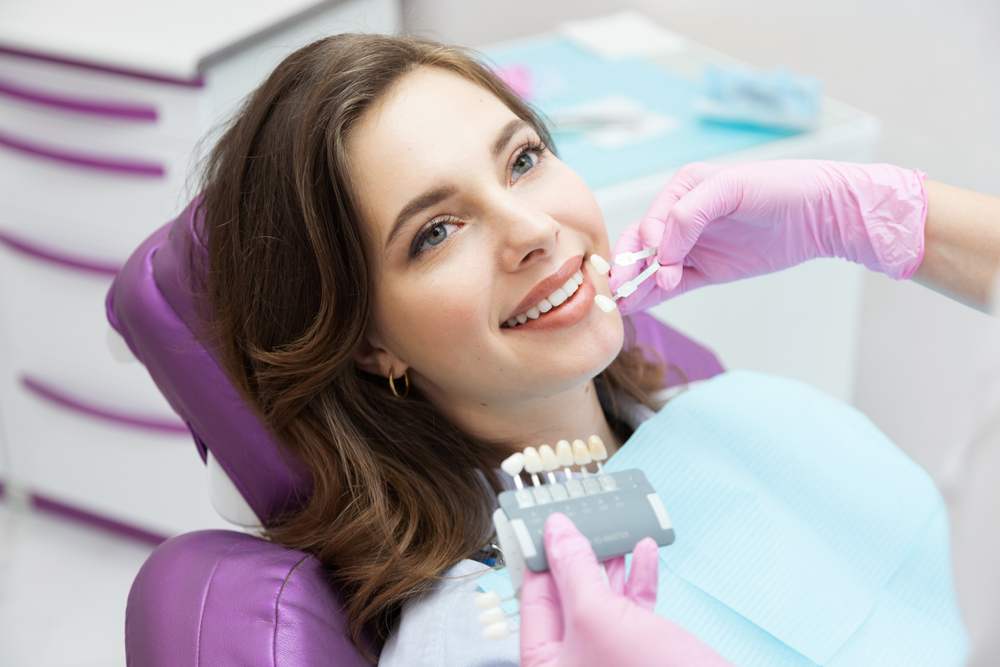 Dentist matching a tooth shade guide to a smiling patient's teeth – BDMS Wellness Clinic