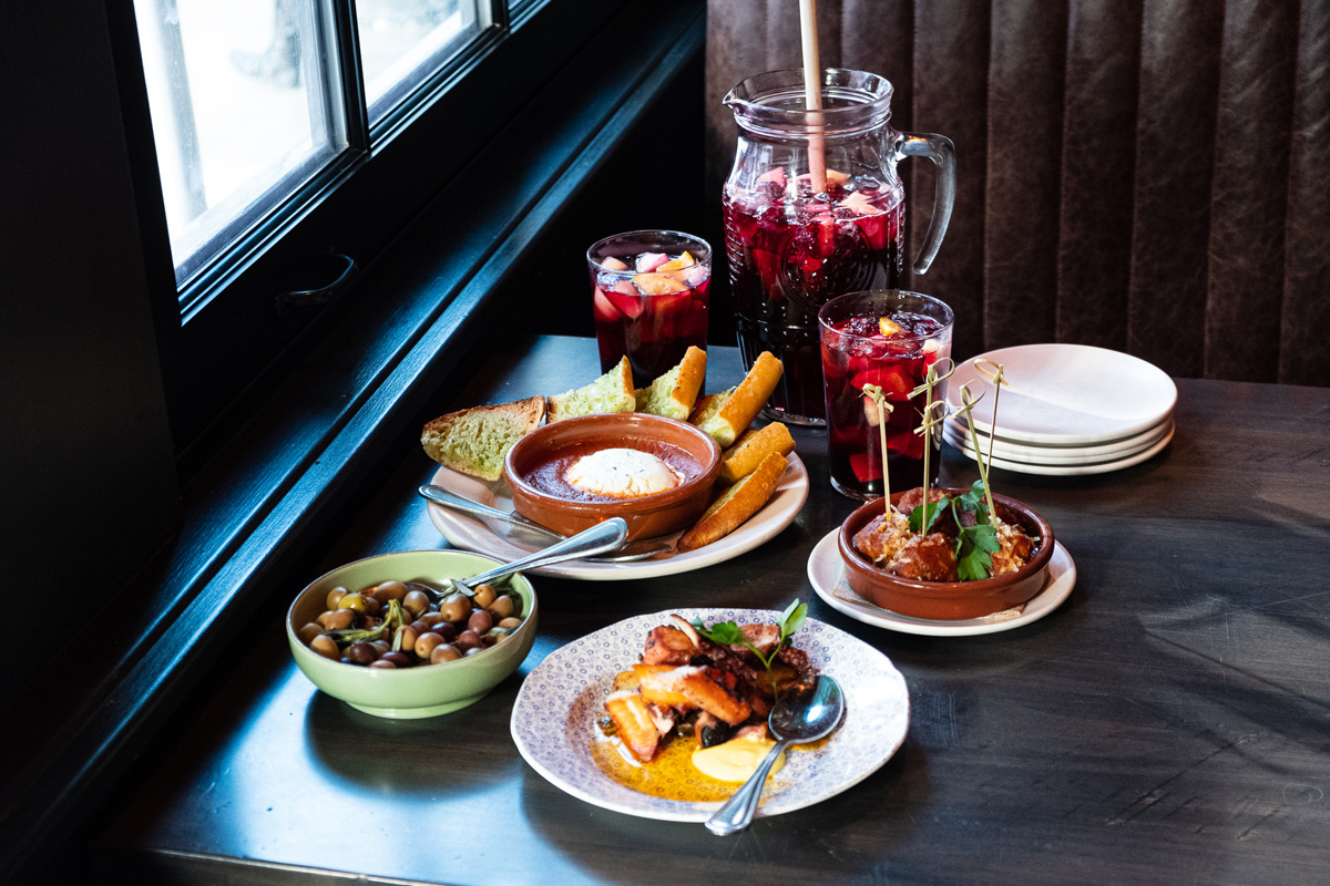 Pitcher of sangria and a selection of tapas (baked goat cheese, house-marinated spanish olives, spanish meatballs “al jerez,” spanish octopus & potatoes) on a wood table