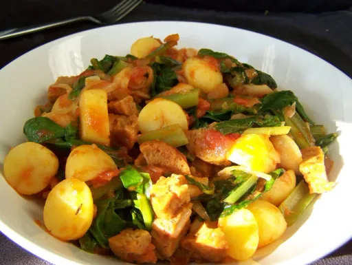 Plato de espinacas y tomate con salchicha vegetariana y patatas
