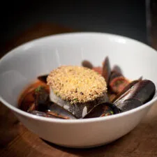 Merluza con costra de polenta, mejillones, chorizo y garbanzos