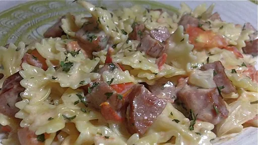 Comida a la sartén de pasta cremosa, salchicha y tomate