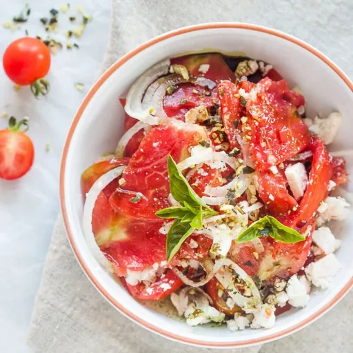 Ensalada de tomate con queso feta, cebolla y aceite de semilla de calabaza
