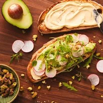 Tostada contundente de hummus con aguacate, rúcula y pistachos