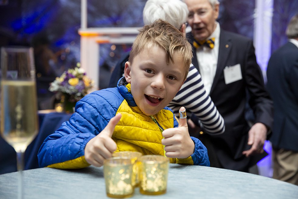 Photo of a young boy dressed in blue and gold, giving the camera two thumbs up