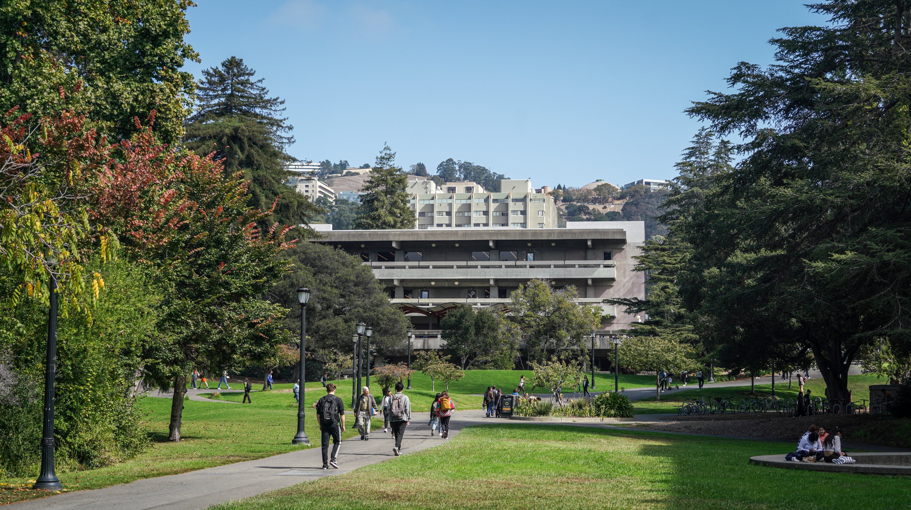 Photo of Moffitt under a blue sky, surrounded by trees and passersby