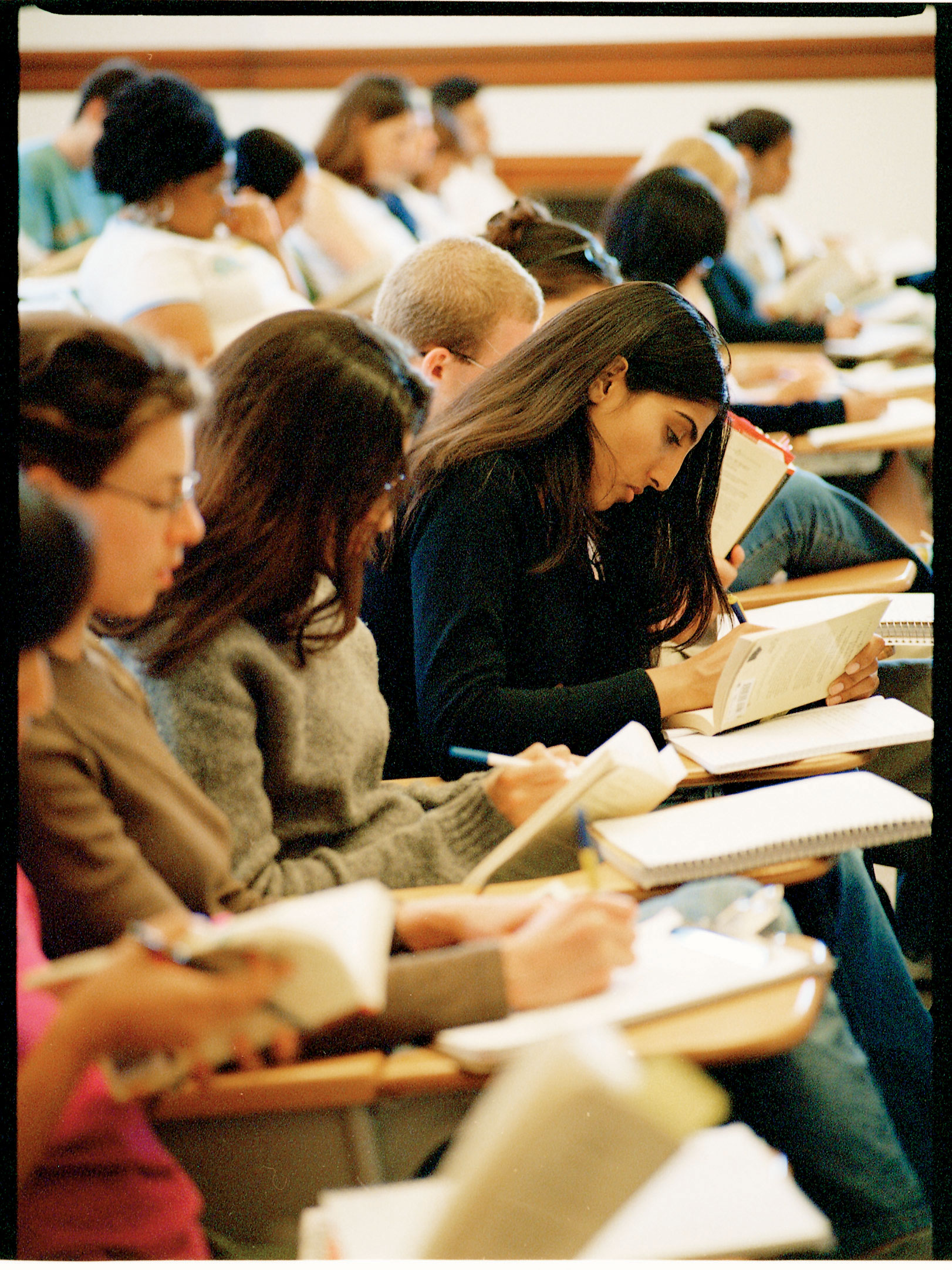 Close-up of a row of students highlighting pages in books, one woman's face particularly visible in profile