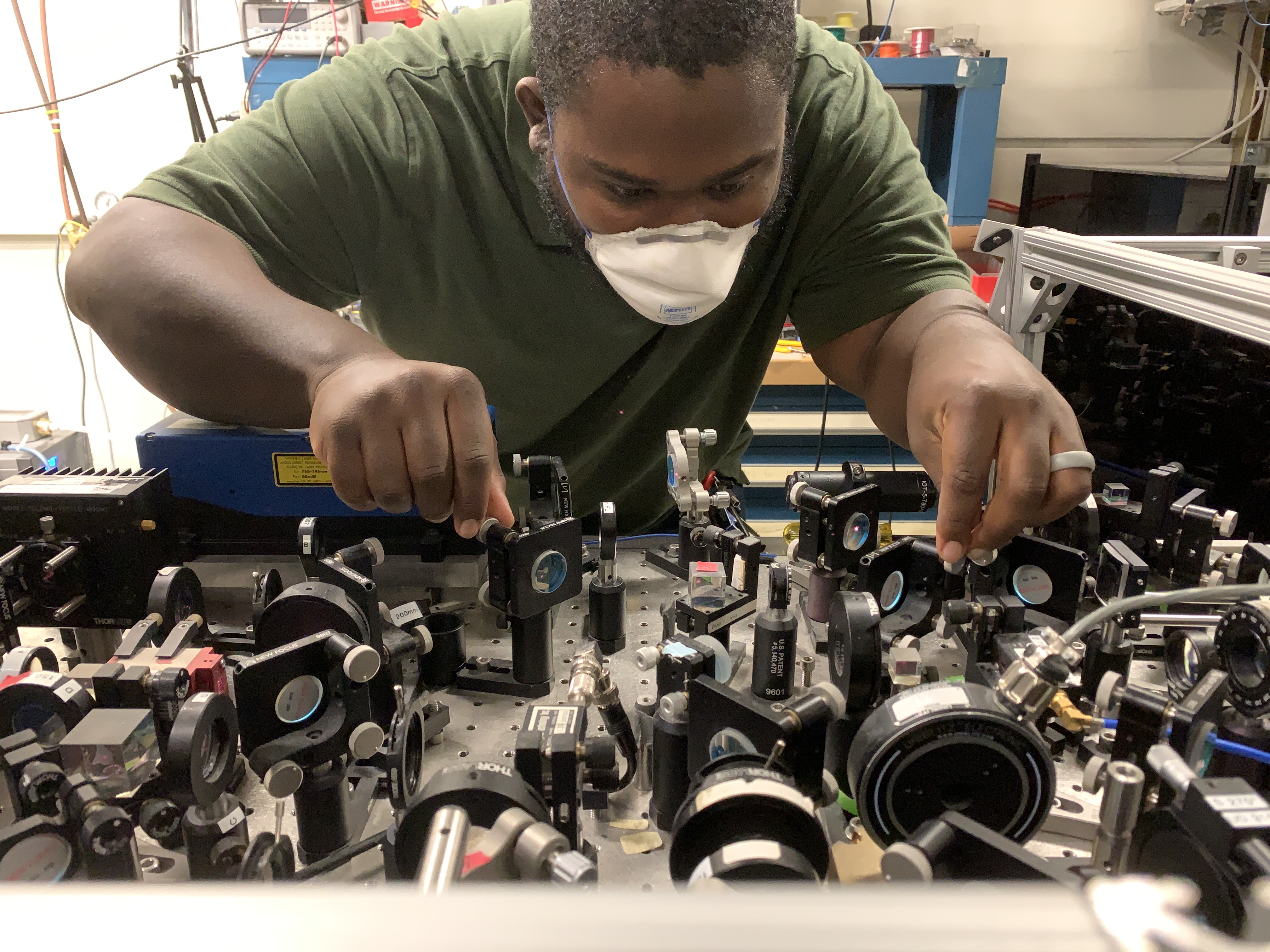 Photo of Charles in  a green shirt wearing a mask and working over a table full of equipments