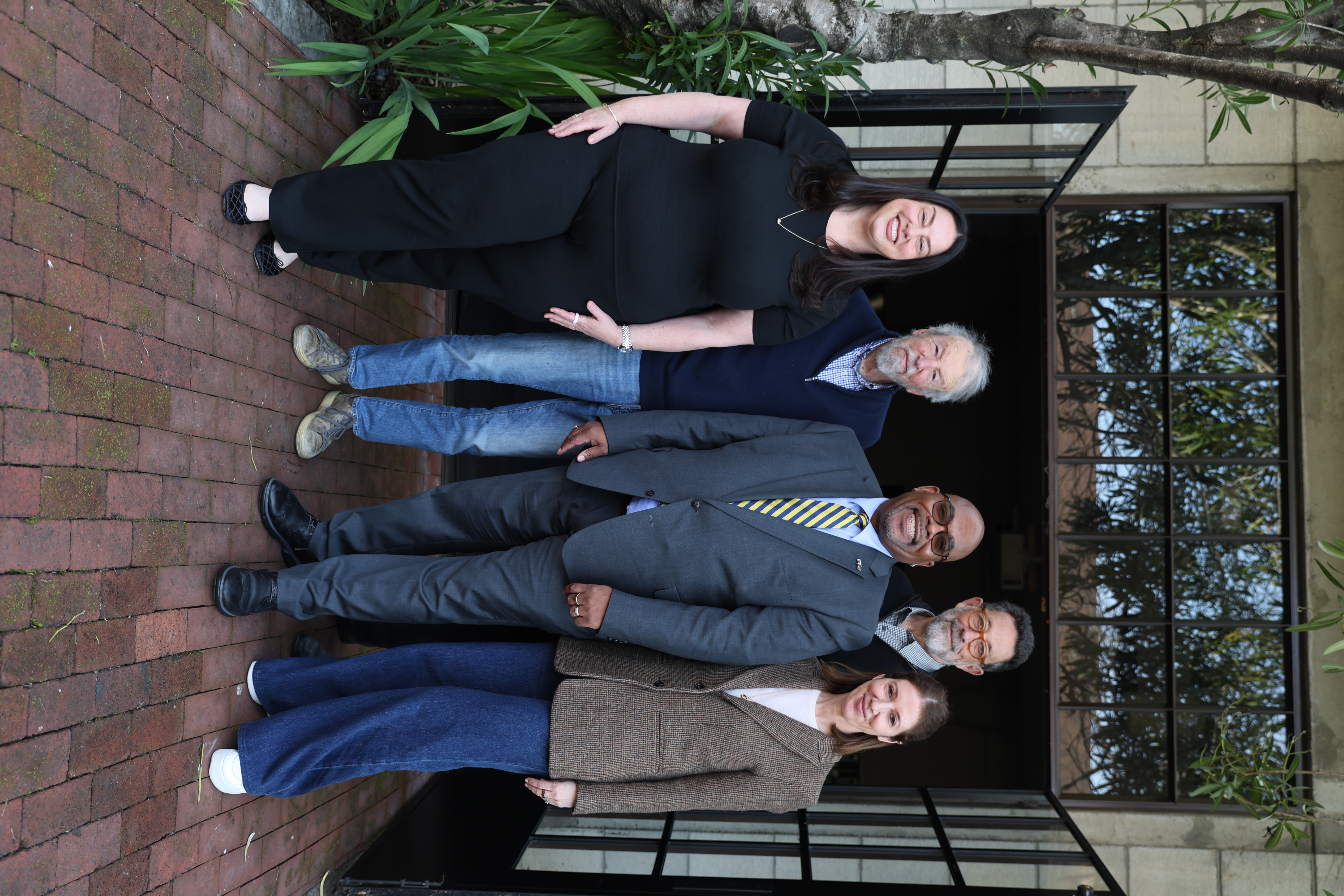 Color photo of four people on campus, smiling at the camera.