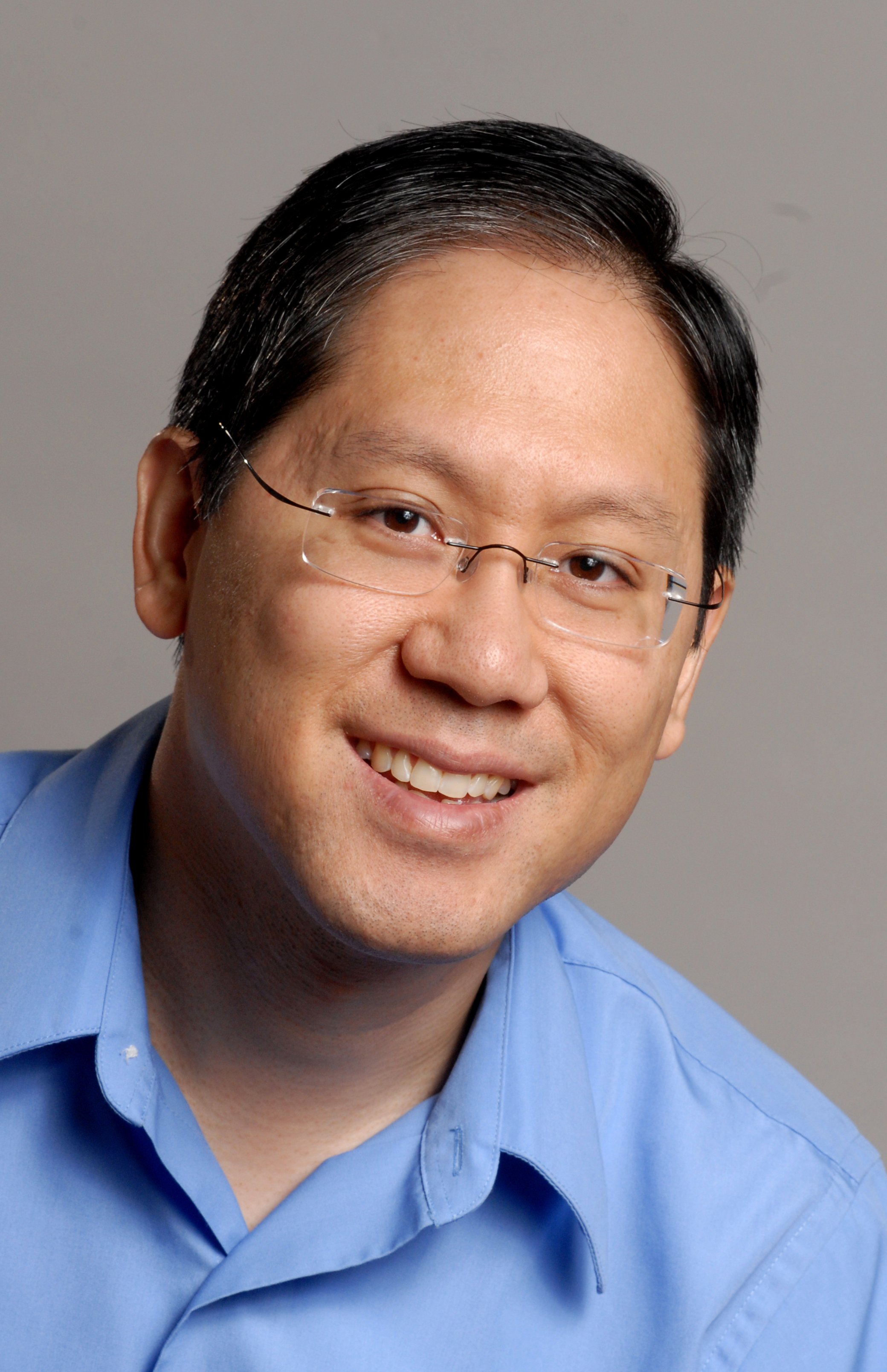 Headshot of Clark against a neutral gray background, leaning to his left wearing glasses and a blue shirt.