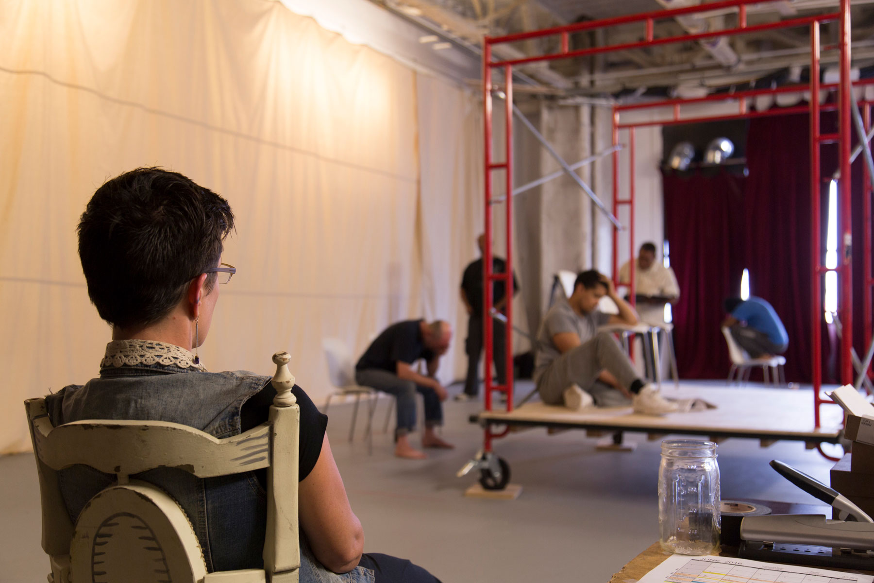 Photo of the back of Shourd looking on as several members of the cast rehearse a scene.