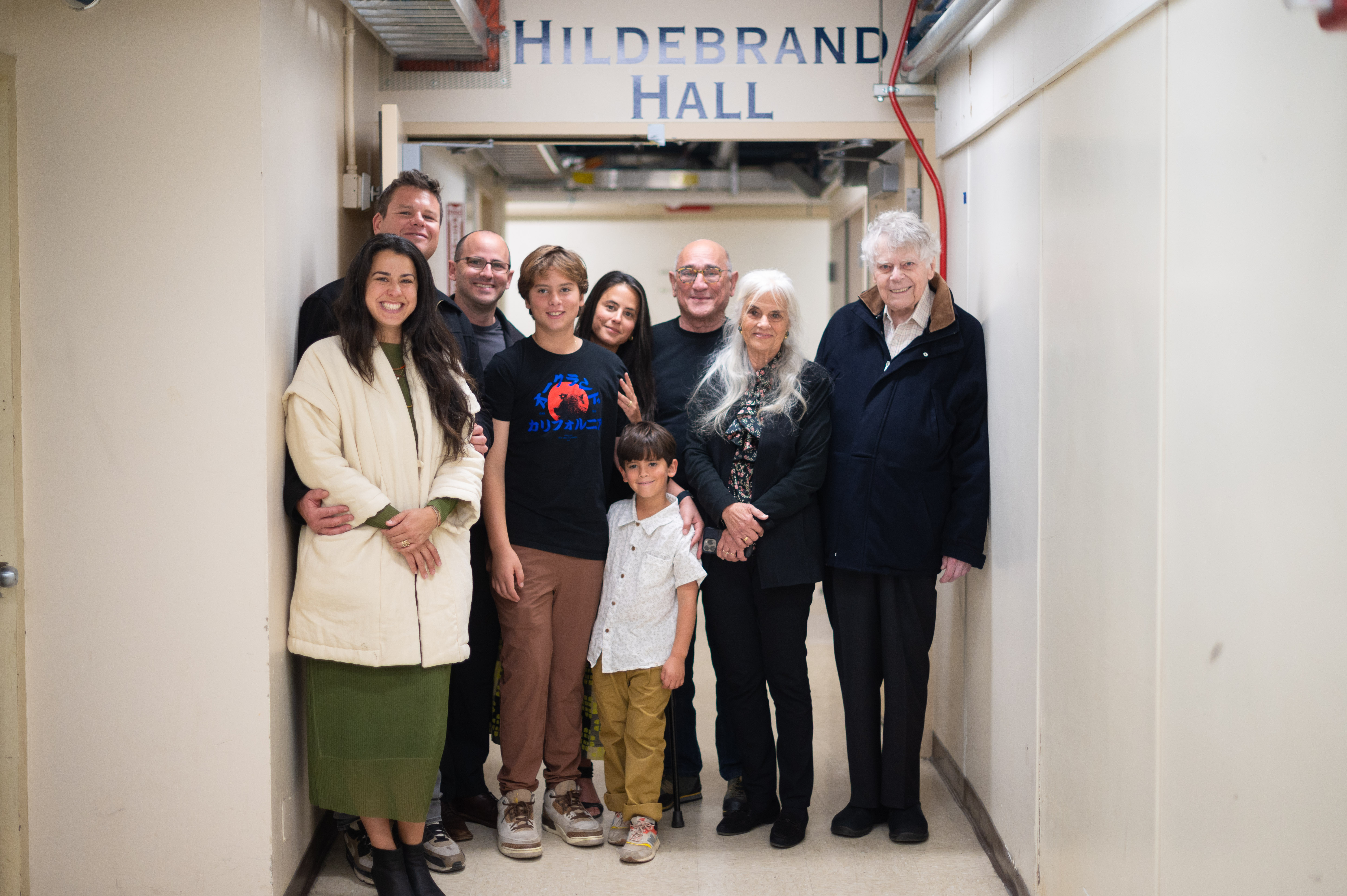 Photo of Alex with eight members of his family stand in a white hallways, with a sign for Hildebrand Hall hanging above.