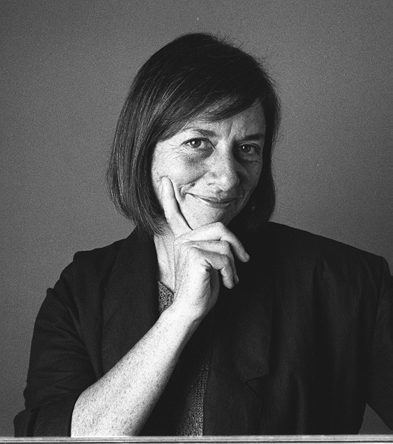 Black and white photo of a woman smiling sardonically at the camera, her chin in her hand.