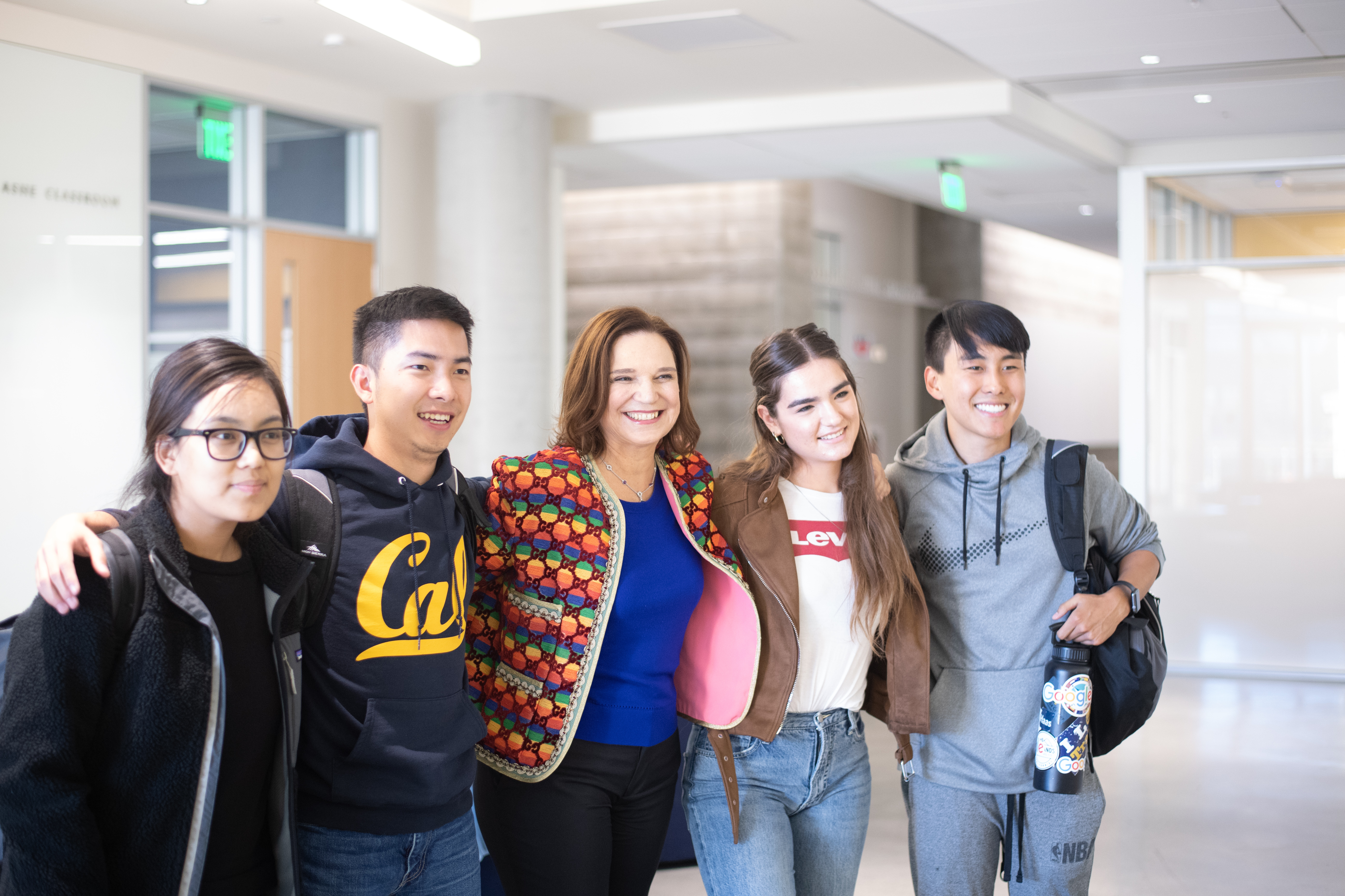 Photo of Dean Harrison in a brightly patterned jacket featuring the colors of the rainbow, flanked by two students on each side of her.